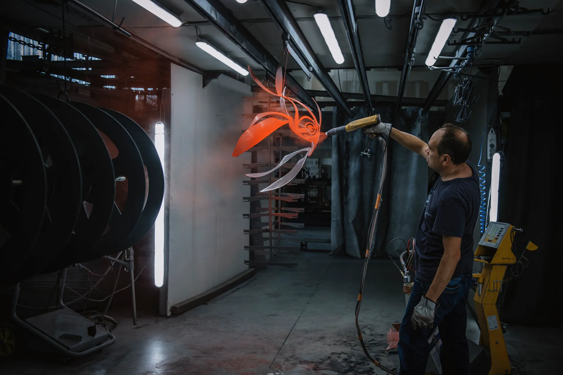 l'artiste projetant de la peinture orange à l'aide d'un pistolet sur un poisson de métal