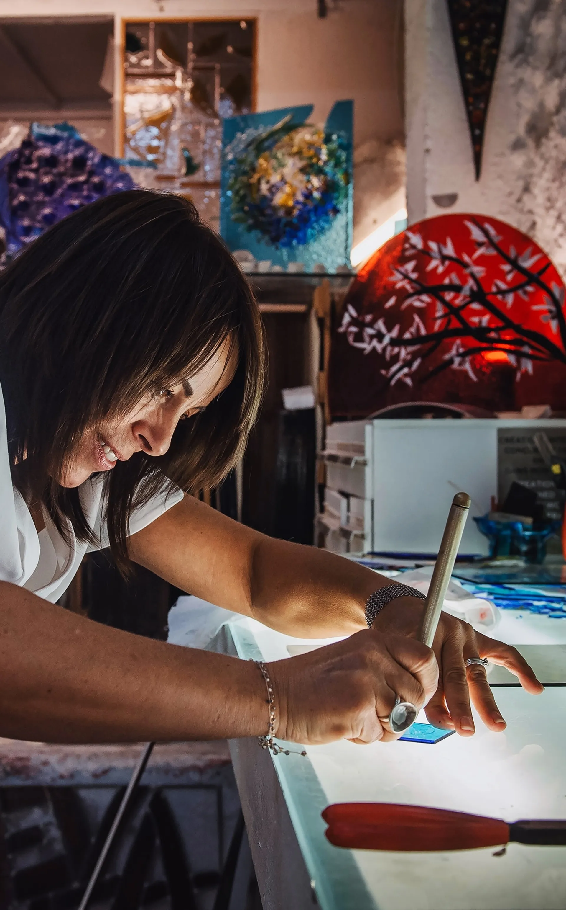 portrait de l'artiste Eva Luca découpant une pièce de verre bleu sur une table lumineuse