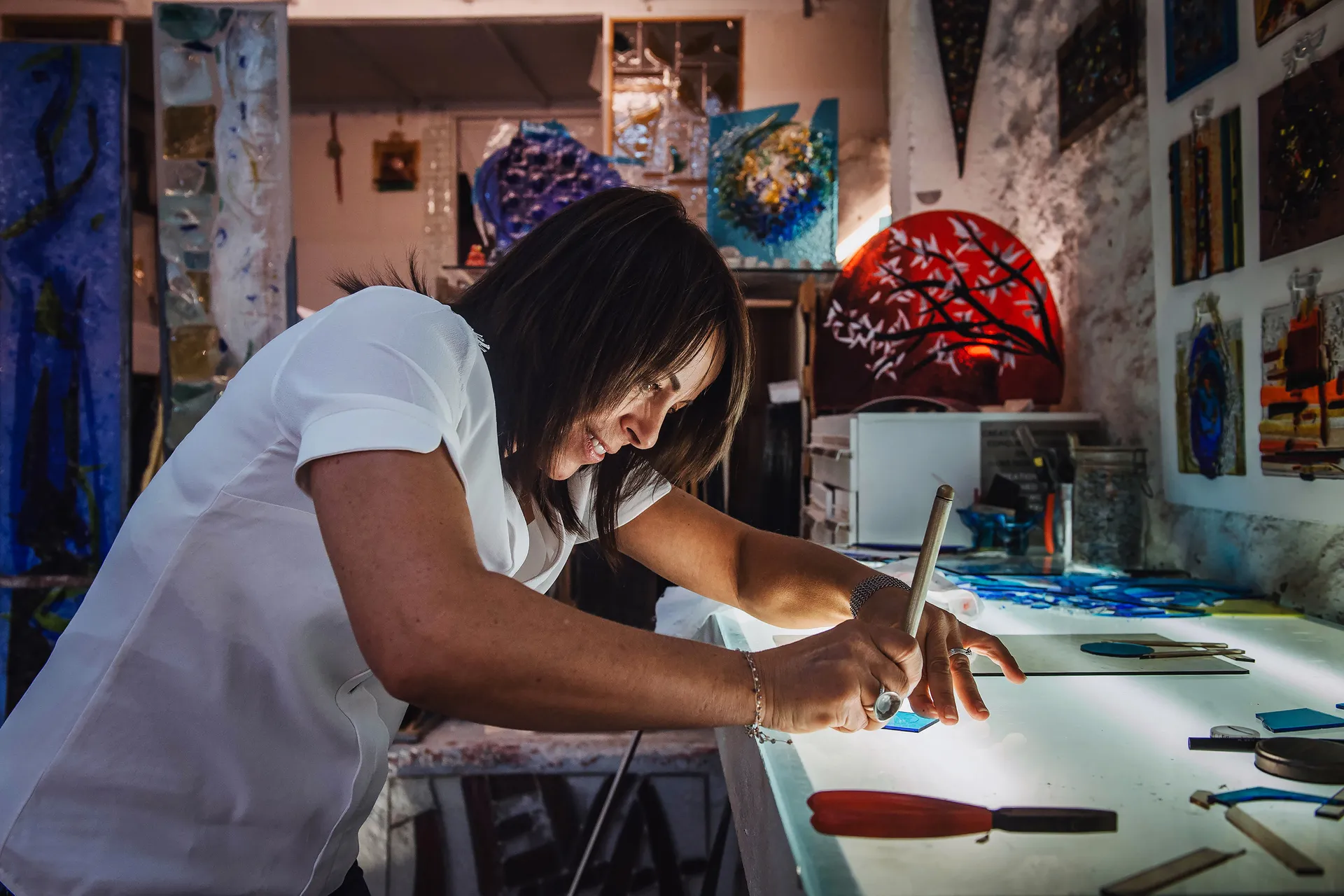 portrait de l'artiste Eva Luca découpant une pièce de verre bleu sur une table lumineuse