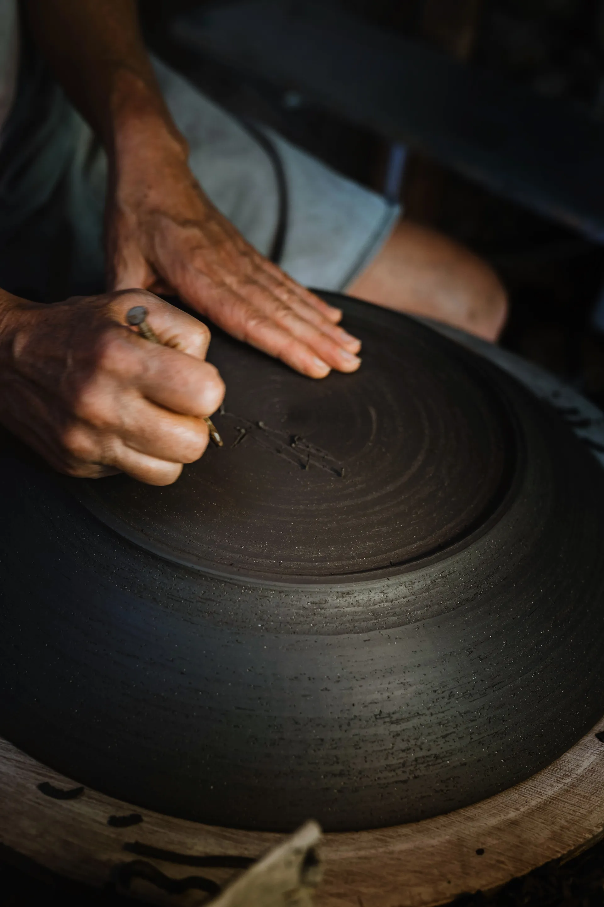 l'artiste gravant sa signature sous le fond d'un grand plat en terre